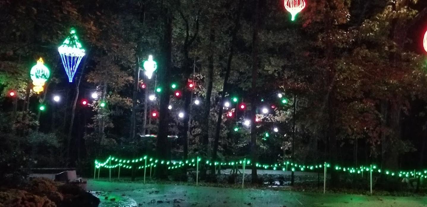 A dramatic outdoor lighting display with glowing trees, colorful illuminated accents, and reflective water features creating a magical nighttime scene.