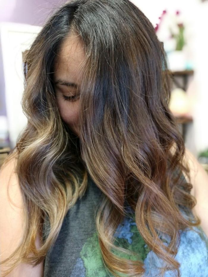 Long brunette hair with warm caramel balayage, beachy waves, and natural movement for a sun-kissed style.