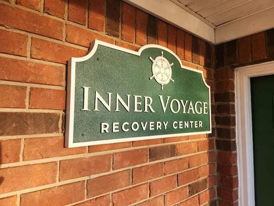 Green and white exterior sign reading "INNER VOYAGE RECOVERY CENTER" mounted on red brick wall, nautical compass logo, attached to building exterior.
