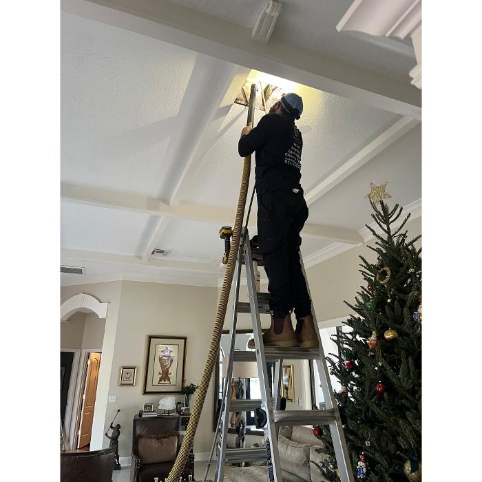 Clean Air Pros technician using specialized tools to clean an overhead air vent in a home with high ceilings.