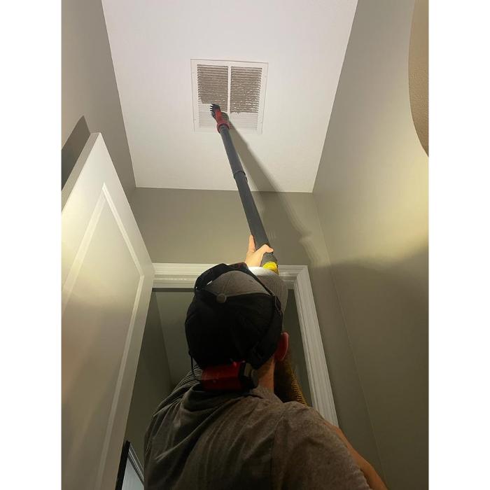 Clean Air Pros technician using specialized equipment to clean an overhead air vent, improving indoor air quality and HVAC performance.