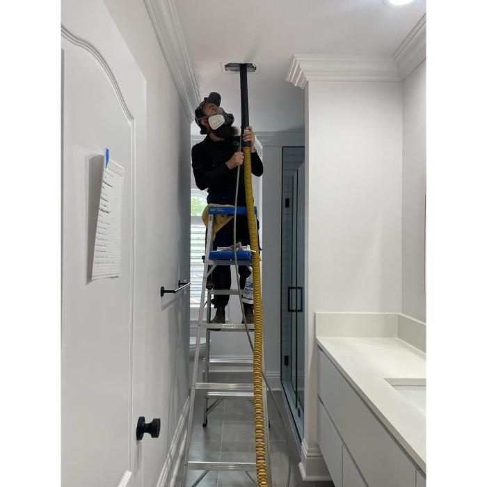 HVAC professional on a ladder cleaning or inspecting an overhead vent as part of a residential duct cleaning service.