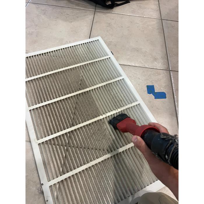 Technician cleaning a reusable air filter to remove dust and debris and help improve airflow and HVAC efficiency.