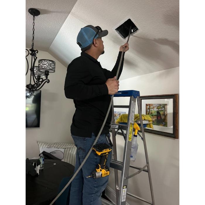 HVAC professional servicing an overhead vent as part of a residential air duct cleaning and maintenance visit.