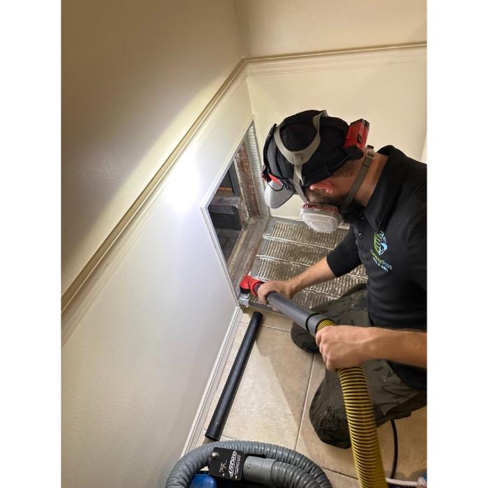 Clean Air Pros FL technician using specialized tools to remove dust and debris from residential ductwork in a narrow access space.