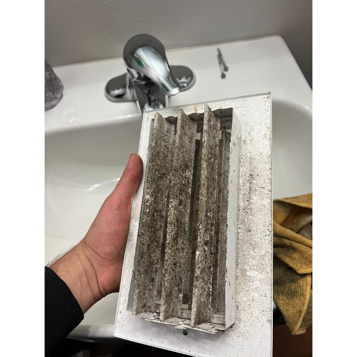 Close-up of a removed air vent cover with heavy dust buildup, showing why regular vent cleaning is important for healthier indoor air.
