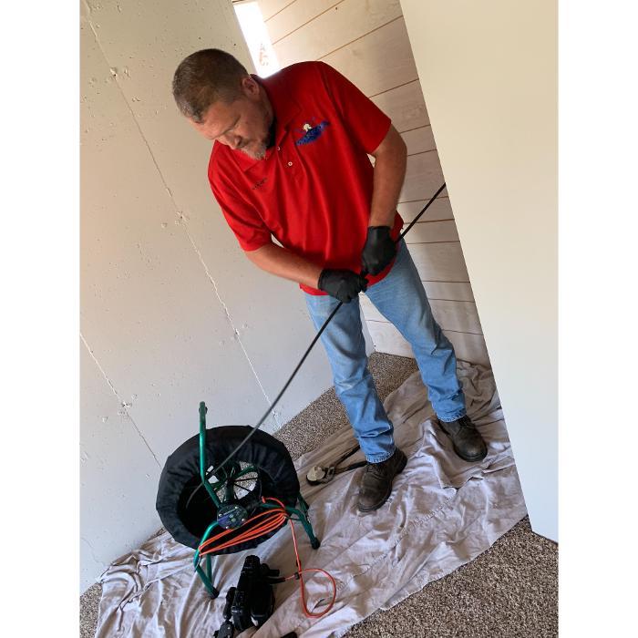 Licensed plumber performing sewer camera inspection with professional drain snake equipment.