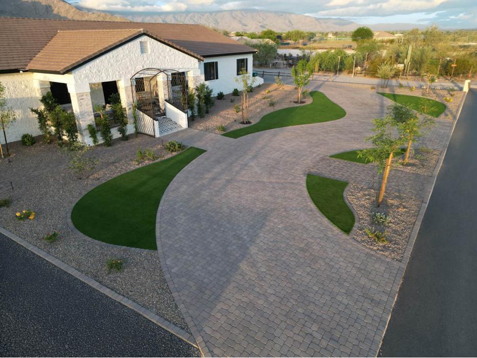 Full desert landscape transformation with a curved paver driveway, xeriscape gravel beds, and integrated artificial turf for a modern Arizona home.