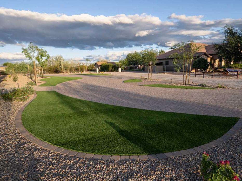 Custom shaped artificial turf lawn bordered by decorative desert gravel and mature trees for a modern, low maintenance Arizona front yard.