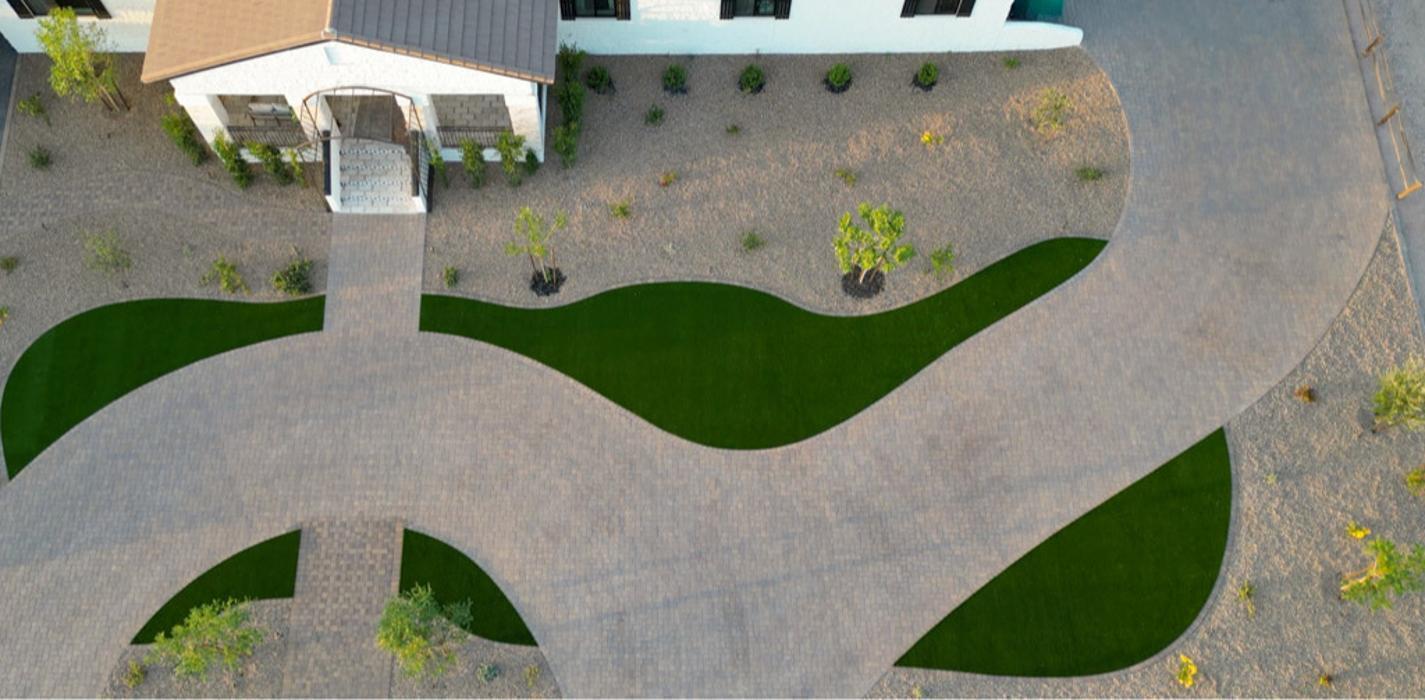Drone view of a full front yard transformation featuring a paver driveway with custom artificial turf wave accents.