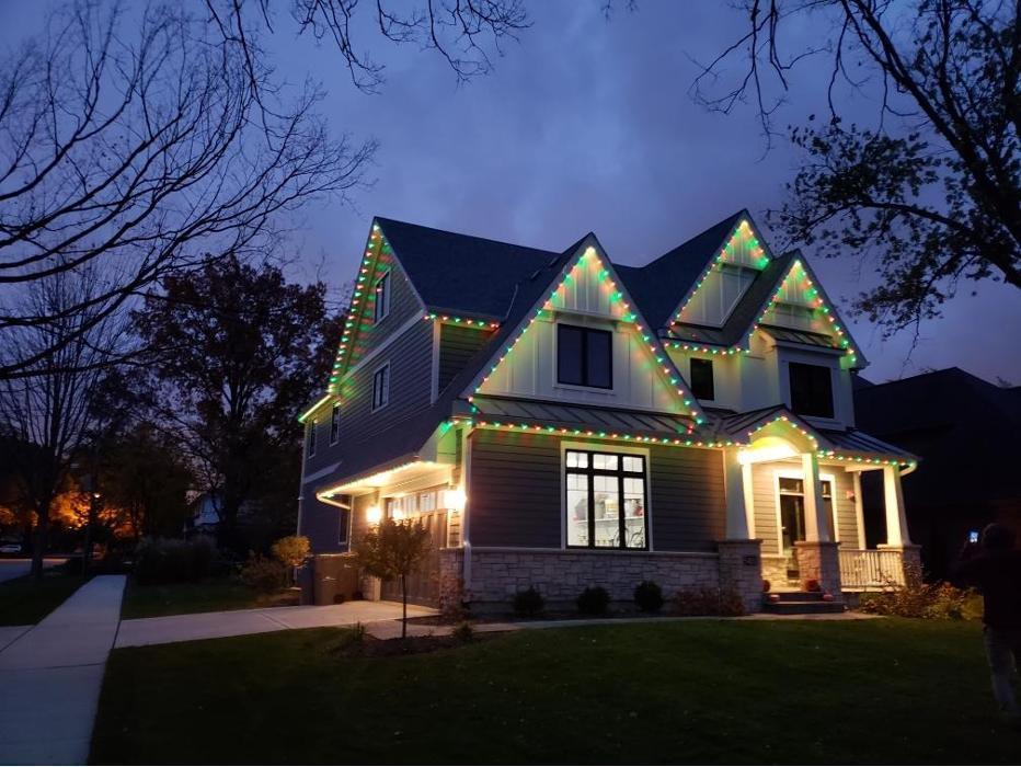 A beautiful custom home in Western Springs featuring professionally installed permanent holiday lighting by Trimlight Chicago. The roofline, peaks, gables, garage, and front porch are outlined with vibrant red and green LED lights.