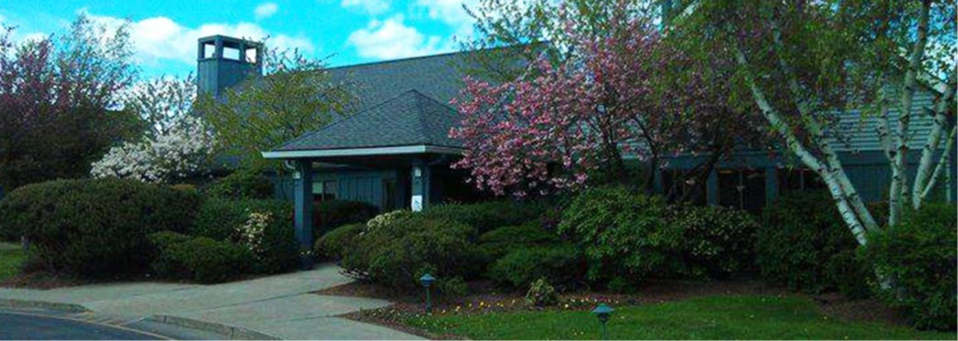 Arms Acres inpatient addiction treatment and drug and alcohol detox center in Carmel Hamlet, New York, surrounded by landscaped shrubs, trees, and flowering plants.