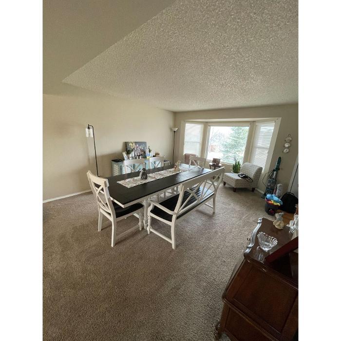 Clean, tidy dining room with large table, bright bay window, and carpeted floor in a Colorado Springs home.