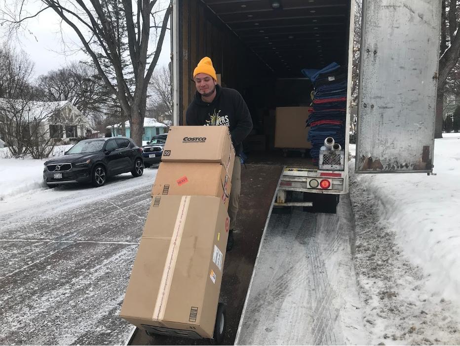 Daymakers Moving & Storage mover unloading boxes from a truck on a snowy Bloomington, MN street.