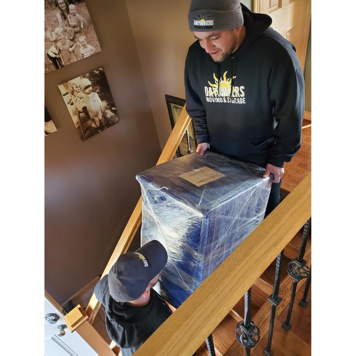 Daymakers Moving & Storage movers carry a wrapped item down stairs in a Lake Elmo, Minnesota home.