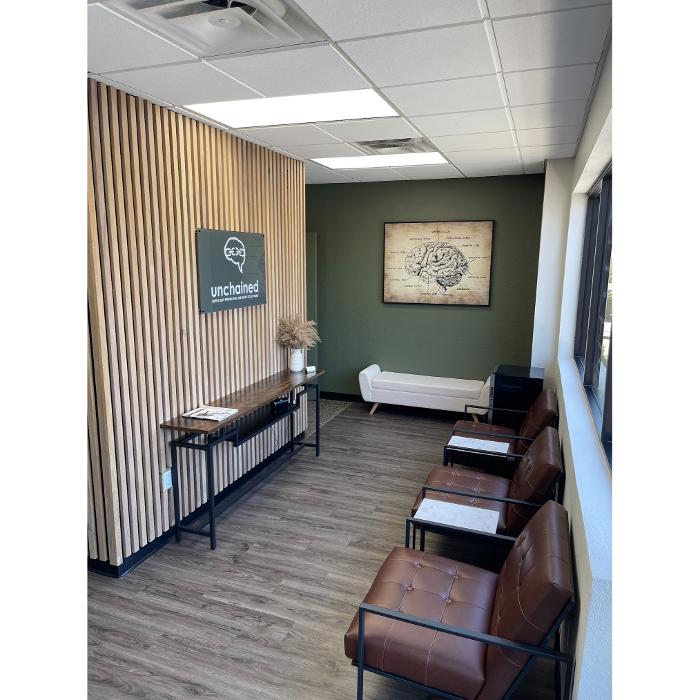 Waiting room at Unchained Psychiatry & Wellness in Gilbert, AZ with chairs, wood wall, and brain artwork.