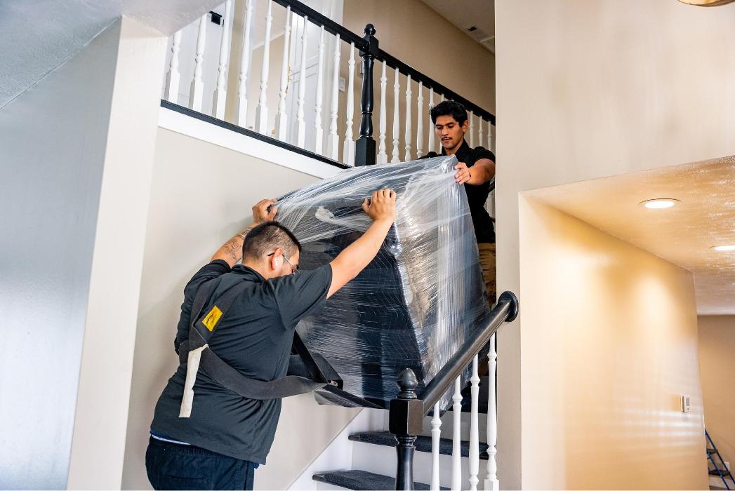 Movers carrying wrapped furniture down stairs inside a Salt Lake City home