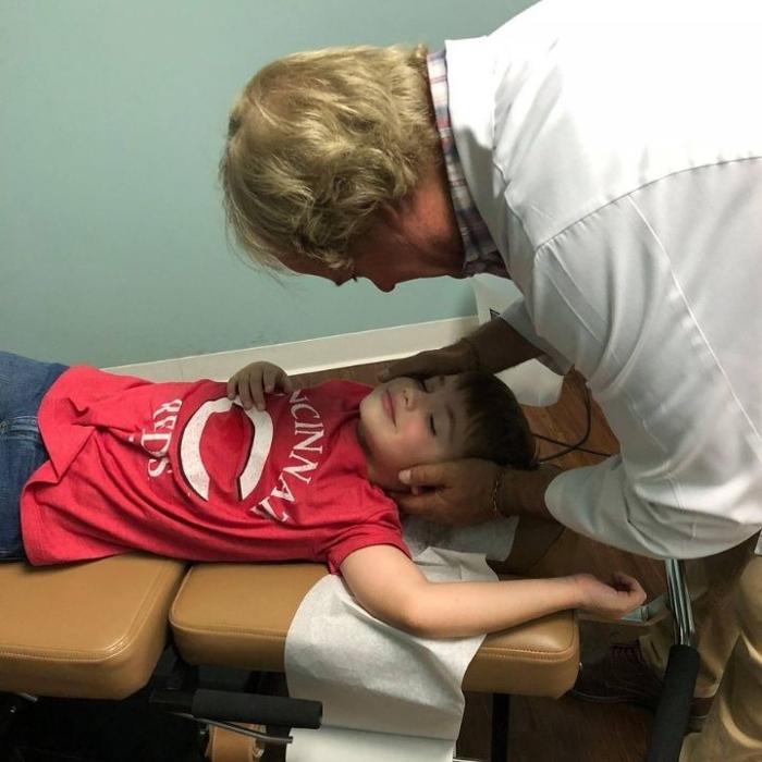 Dr. Reed Moeller works with a young patient wearing a Cincinnati Reds shirt during a pediatric chiropractic visit at Forest Park Chiropractic & Acupuncture in Cincinnati, Ohio.