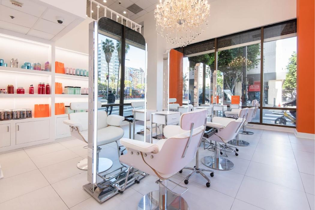 Interior of Logunova Beauty Salon in Los Angeles with white styling chairs, mirrors, chandelier, and product shelves
