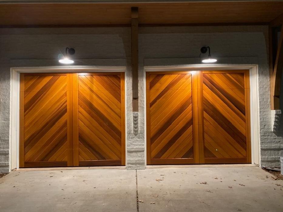 Warm wood double garage door illuminated at night, showing professional installation quality — Hawk Garage Doors