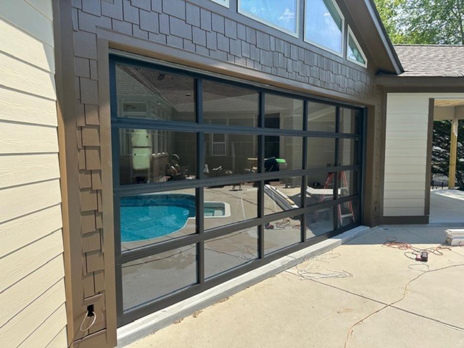 Black aluminum-frame glass garage door with multiple window panels installed on a residential driveway — Hawk Garage Doors