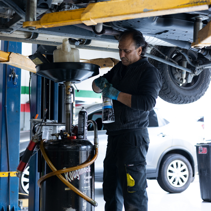 Expert mechanic, Amir, holding a liquid substance in a bottle as he works on a Japanese Auto Repair customer vehicle