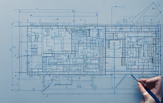 Architektenentwurf auf Tisch mit Zeichengeraeten und Hand, die auf Bereich zeigt.