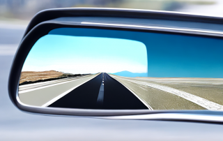 Nahaufnahme eines Rueckspiegels eines Autos mit verschwommener Strasse, Fokus auf sicherem Fahren, Hintergrund mit malerischer Landschaft.