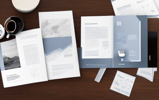 Verschiedene Versicherungsbroschueren und Booklets auf Holztisch mit Laptop und Kaffeetasse, symbolisieren detaillierte Recherche und Vergleich.