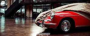 Fahrzeuggaragen von softgarage Ein roter Porsche steht halb abgedeckt mit einer Fahrzeuggarage von Softgarage in einer großen Halle