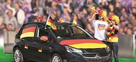 Jubelnde Fußballfans neben Auto.