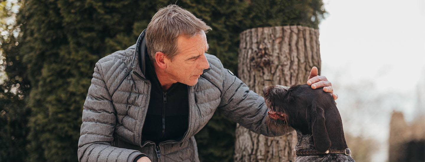 Mann streichelt alten Hund im Garten.